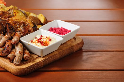 big wooden board with pork ribs and steaks baked in mustard sauce, small sausages, baked potato, grilled tomatoes and onion, hot sauce and horseraddish sauce, preferably served as companion for beer or other alcohol drinks