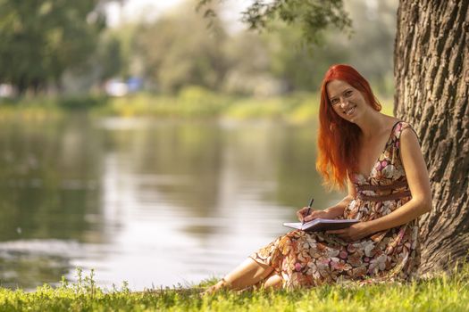 Young redhead woman writing in summer park