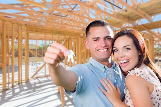 Young Military Couple On Site With House Keys Inside Their New Home Construction Framing.