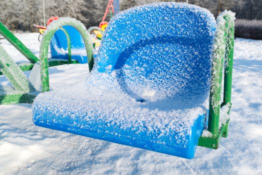 snow covered swing and slide at playground in winter