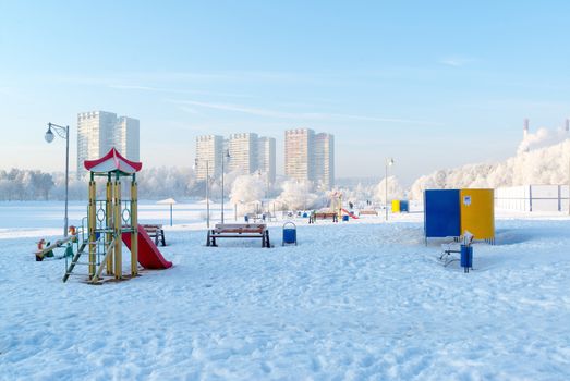 snow covered swing and slide at playground in a winter