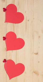 Three hearts with clothes pegs and red paper hearts on a cord on wood