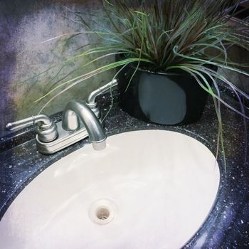 Bathroom sink with metal faucet, decorated with artificial plant.
