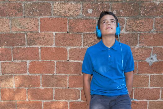 Teenager leaning against a red brick wall, listen to music with headphones.