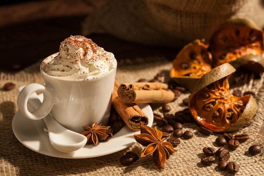 Close-up of a cup of coffee with whipped cream, cocoa powder, cinnamon, star anise and dried orange fruit