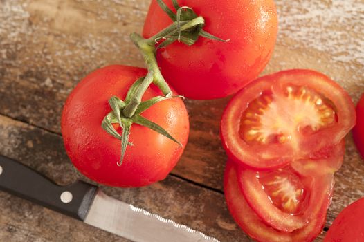Sliced and whole fresh juicy ripe red tomatoes on the vine viewed from above on a rustic wooden table with a kitchen knife alongside