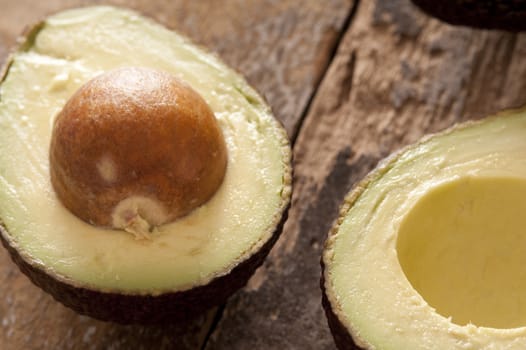 Halved fresh ripe avocado pear with the stone still in viewed close up on a rustic wood background