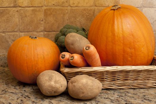 Harvest of fresh fall or autumn vegetables in a shallow wicker basket on a granite counter including carrots, potatoes, broccoli and pumpkins
