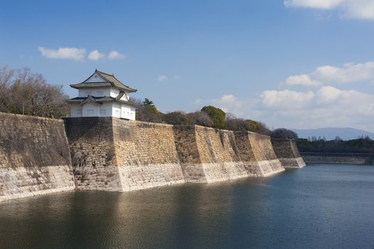 Exterior walls of the Osaka-jo castle, Japan with a small pagoda overlooking the calm water of the surrounding moat, a popular tourist attraction and museum