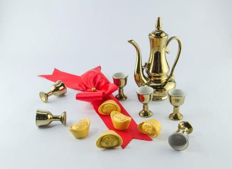 Gold ingot Red ribbon bow Gold jug Tea glass on white background.