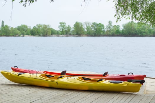 Two kayak boats on wooden deck at kayak station near river bank