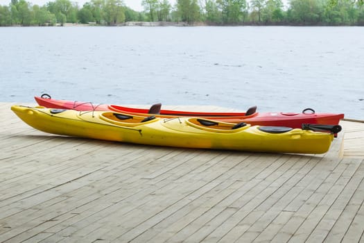 Two kayak boats on wooden deck at kayak station near river bank