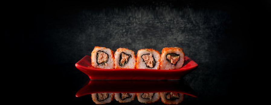 Rolls with tuna on a red dish and black background