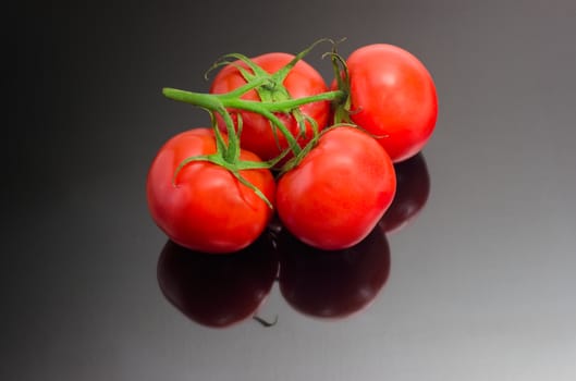 Branch of the ripe red tomatoes closeup on a dark matt reflective surface
