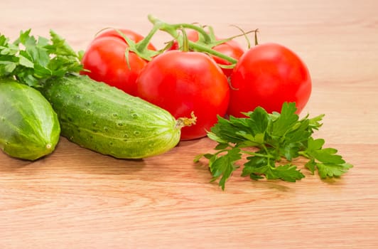 Branch of the ripe red tomatoes, two cucumbers and parsley twigs closeup on a wooden surface
