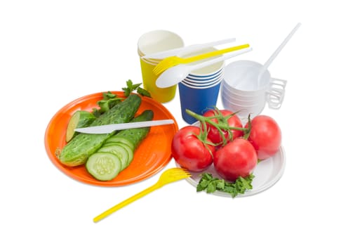 Orange and white disposable plastic plate with whole and sliced cucumber, cluster of the tomatoes, forks, spoons and knifes, paper and plastic disposable cups beside on a light background
