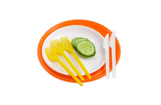 Orange and white disposable plastic plates different sizes and several slices of the cucumber on them, plastic disposable yellow  forks and white knives on a light background
