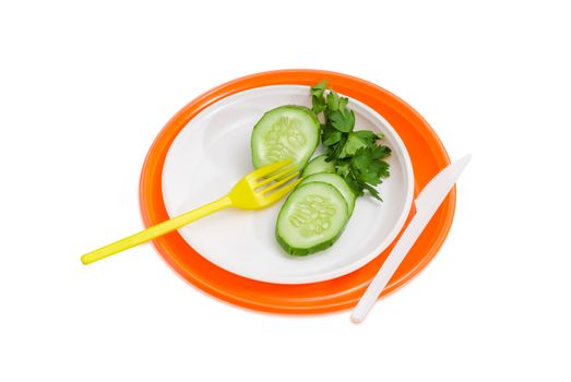 Orange and white disposable plastic plates different sizes and several slices of the cucumber, twig of the parsley, plastic disposable fork and knife on them on a light background
