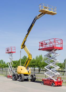 Two scissor wheeled lifts and one wheeled articulated lift with telescoping boom and basket on an asphalt ground
