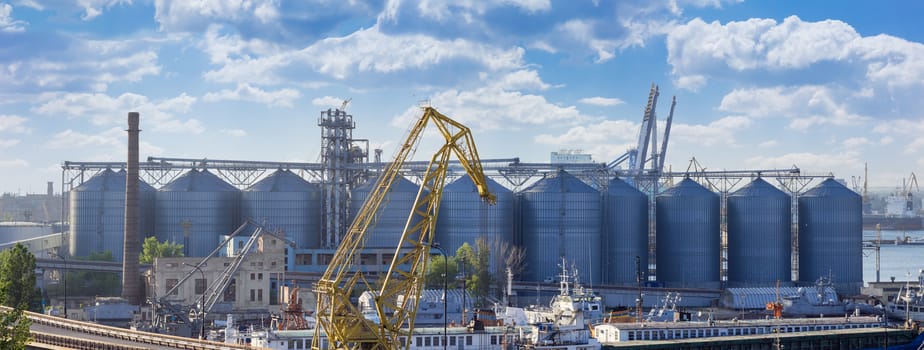 Panorama of the grain terminal with corrugated steel storage bins and grain distribution system in the sea cargo port on the background of sky with clouds
