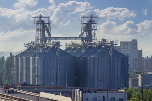 Grain storage system with corrugated steel storage bins and grain distribution system in the grain terminal of the seaport on the background of sky with clouds
