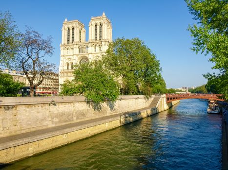 West facade of the Cathedral Notre-Dame de Paris with river Seine and her embankment in the foreground in the spring evening
