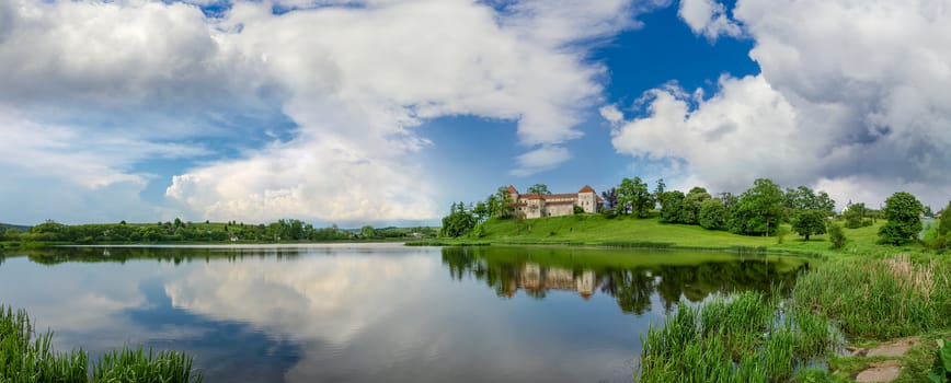 Panorama of pond after a thunderstorm with ancient castle on the opposite bank. Svirzh Castle built in the 15th century, Lviv region, Ukraine.
