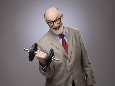 Happy funny senior man in suit with dumbbell, power concept