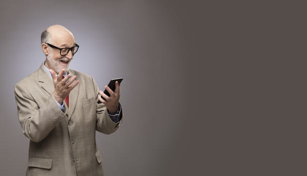 Portrait of funny senior man looking on phone with gray copy space