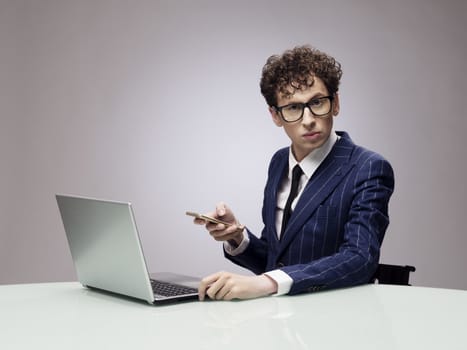 Funny businessman in glasses with laptop and phone, studio shot on gray background