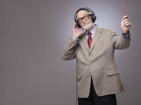 Portrait of senior man in headphones listening music, studio shot on gray background