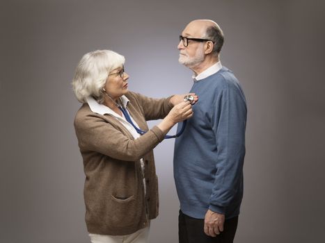 Old couple. Senior woman taking care, checking heart beat of husband with stethoscope