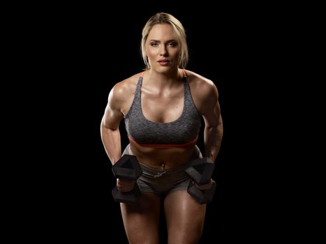 Muscular woman doing exercises with dumbbells for back, isolated on black background