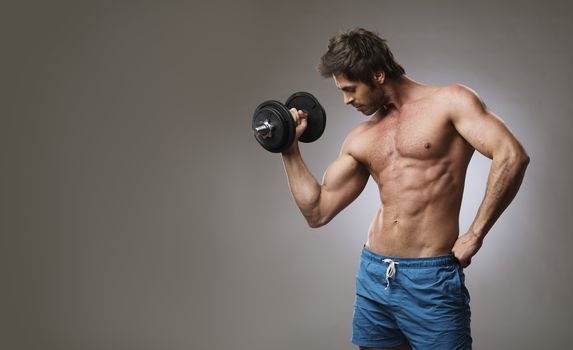 Handsome muscular man with bare chest lifting dumbbell, studio shot on gray background