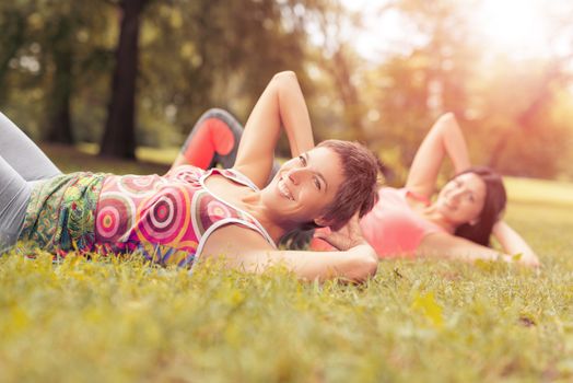 Two beautiful women doing sit-ups exercise in the park. Selective focus.