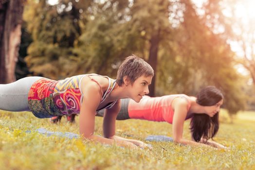 Two beautiful women doing plank exercise in the park. Selective focus.