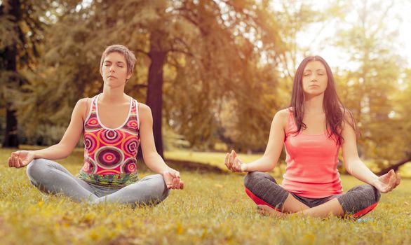 Two beautiful women meditating in the park. 