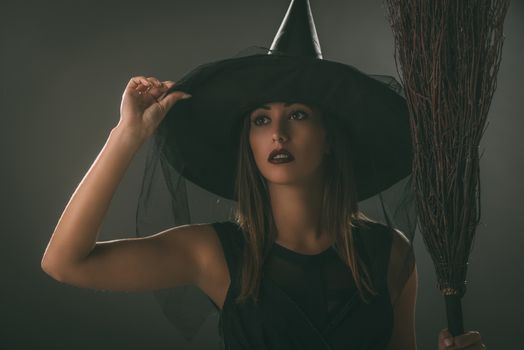 Portrait of a young woman dressed like a witch. She is in dark clothing and holding a broom.