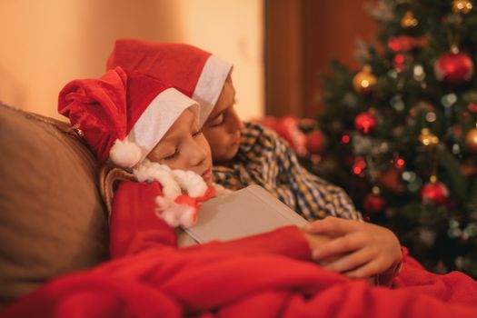 Cute sister and brother sleeping next to a Christmas tree at the home. 