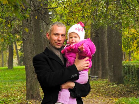 dad in the black coat holds daughter on hands in autumn Park