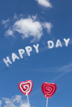 The word Happy Day in the blue cloudy sky and two lollipop