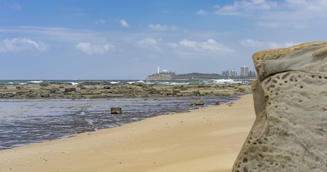 Australian beach panorama with sandy foreground,  rocks, reef, crashing waves, ocean, horizon and blue sky