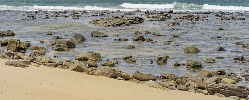 Australian Pacific ocean coastline with sandy beach and rocky shoreline during flood tide panorama view