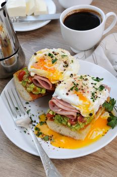 poached  eggs with avocado, tomatoes, slices of ham on a baguette for breakfast