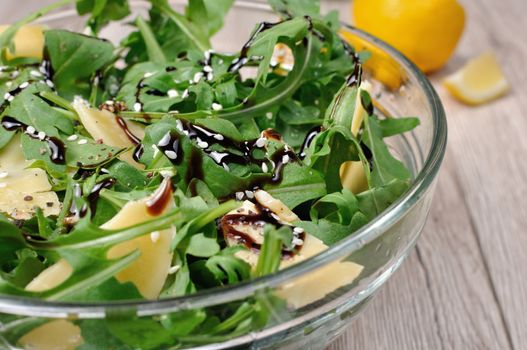 Arugula (rocket) salad dressed with balsamic soy sauce , Parmesan shavings and freshly ground black pepper, sesame.  Horizontal shot.