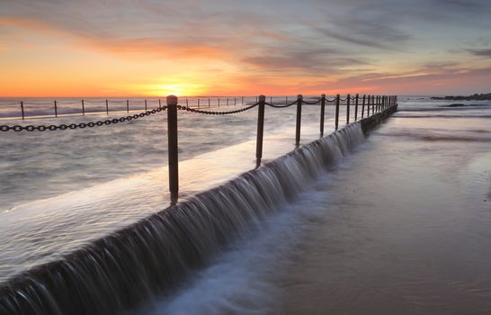 The sun rises at Newport rock pool Australia as excess sea water spills over the pool edge