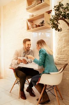 Two beautiful young smiling businesspeople sitting at cafe and working on digital tablet. Selective focus.