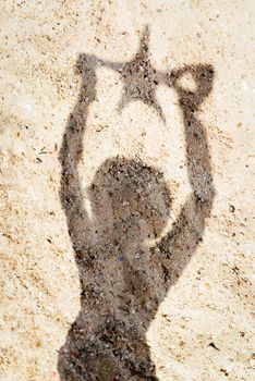 Shadow on sand of a woman holding starfish. 