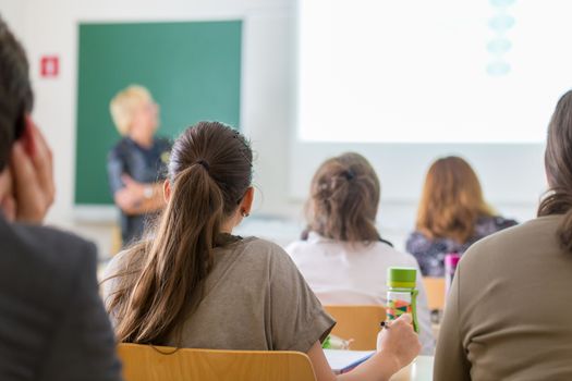 Teacher at university in front of a whiteboard screen. Students listening to lecture and making notes.