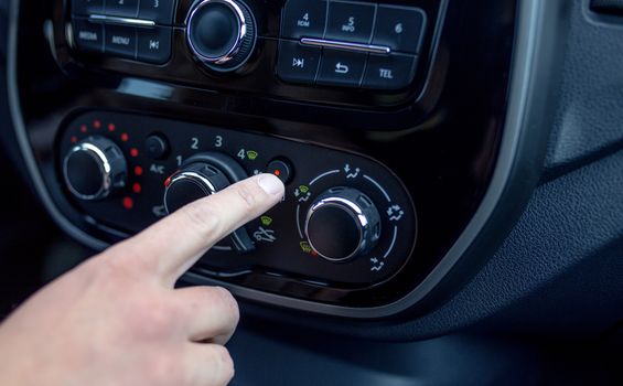 male hand pressing button in modern car. Man adjusts the temperature of the car air conditioner